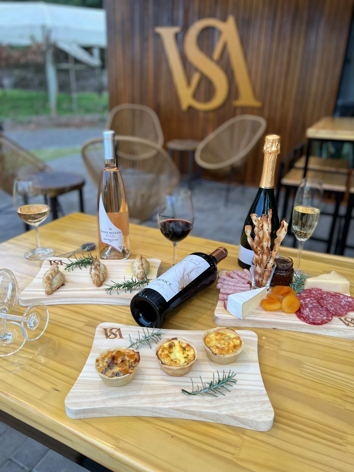 Mesa com vinhos e gastronomia, com a marca VSA ao fundo no Wine Garden